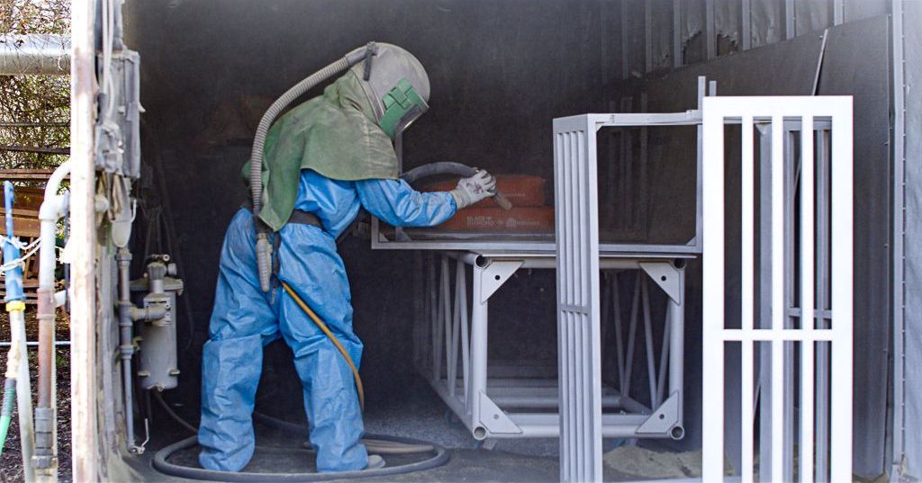 Colortec technician in a blast hood removing debris from a metal frame
